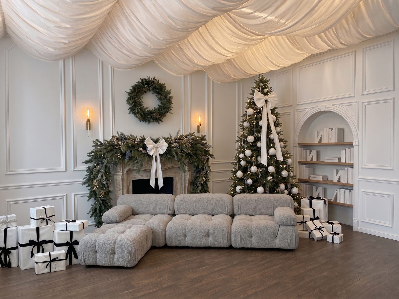 The Blanc Set 2026 — draped ivory ceiling, garland fireplace, white-ornament tree and bouclé sofa